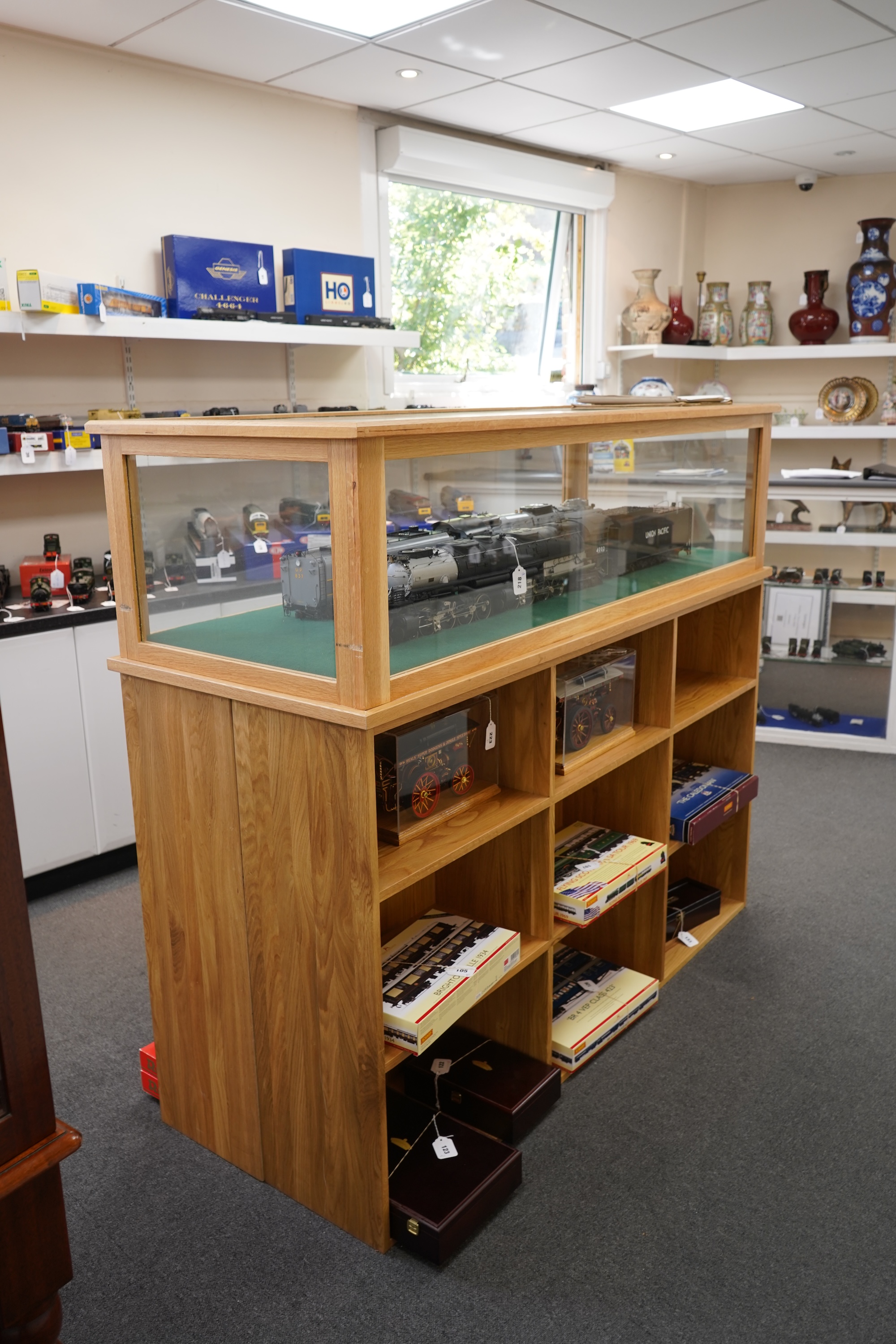An engineered oak display stand, with a removable glazed top, and double sided base divided into nine compartments on each side, dimensions; 160cm wide, 60cm deep, 141cm high (contents for display purposes only and not i
